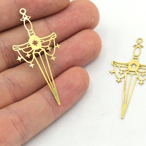 May include: Two gold-toned metal charms in the shape of a sword with a starburst design. The sword has a decorative handle and a pointed tip.