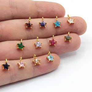 May include: Assortment of gold star charms with various colored crystal accents. The charms are approximately 1 cm in size and are perfect for adding a touch of sparkle to jewelry projects.