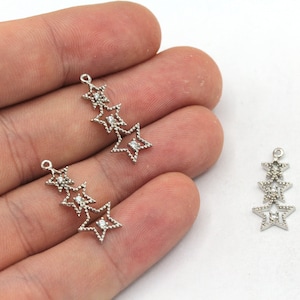 May include: Two silver star charm pendants with clear rhinestones. Each pendant features three layered stars.