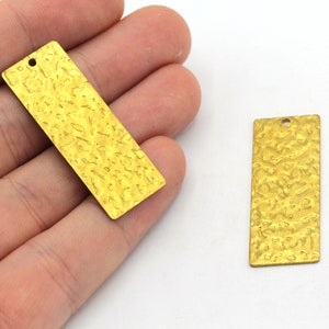 May include: Two gold-colored metal rectangular tags with a textured surface. Each tag has a small hole at the top for hanging.