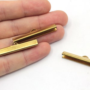 May include: Two gold metal cord end stoppers with a textured surface. The stoppers are designed to hold the ends of cords or straps in place.