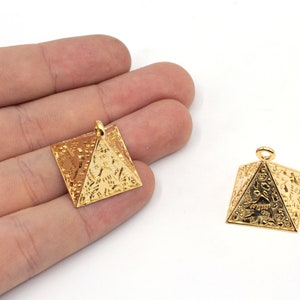 May include: Two gold-colored pyramid-shaped pendants with intricate designs. The pendants have a loop at the top for attaching to a chain or cord.