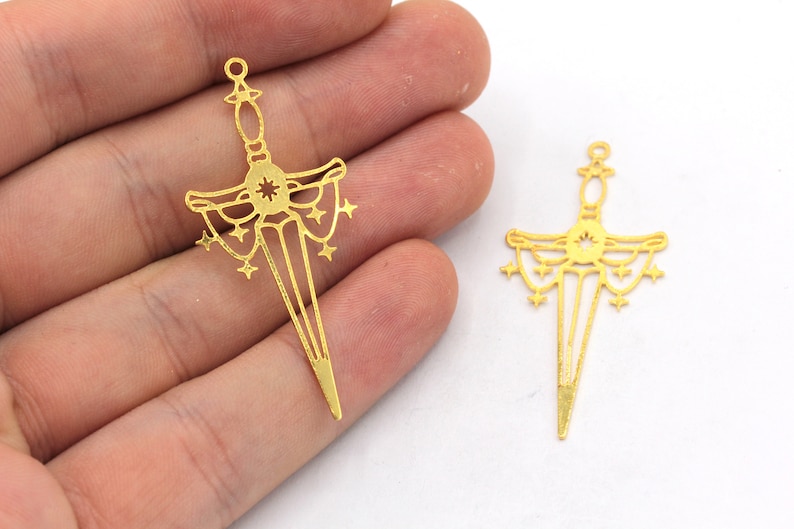 May include: Two gold-coloured metal sword charms with a starburst design and a dangling chain of stars.