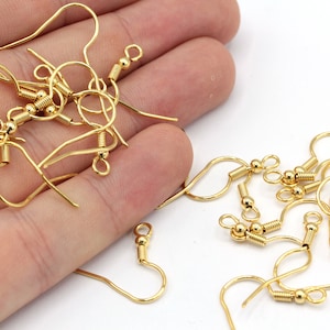 May include: A close-up of a pile of gold-toned earring hooks with spring-loaded closures. The hooks are made of metal and have a smooth, polished finish.