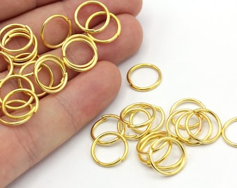 May include: A collection of small, shiny gold-colored jump rings. These circular rings are open and ready to be used for jewelry making or other craft projects. The rings are scattered on a white surface.