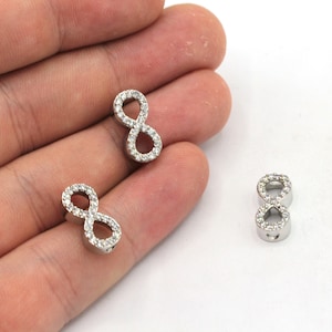 May include: Three silver infinity symbol charms with clear crystal accents. The charms are small and delicate, perfect for adding a touch of sparkle to jewelry.