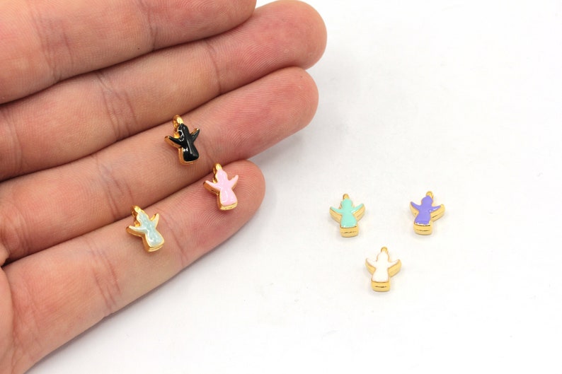 Pode incluir: Cinco pingentes de anjo dourados com tinta de esmalte em diferentes cores: preto, rosa, verde claro, roxo e branco.