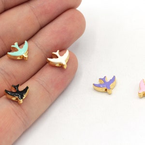 May include: Five gold-coloured bird charms with enamel paint in different colours: light blue, white, purple, pink, and black.