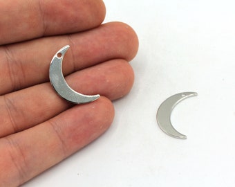 May include: Silver-colored crescent moon charms with a small hole at the top for jewelry making. One charm is held in a hand, and another is on a white surface. These charms are ideal for creating celestial-themed jewelry.