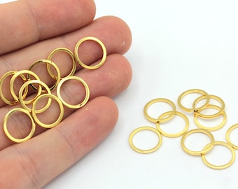 May include: A collection of small, gold-colored metal rings. Some rings are held in a hand, while others are scattered on a white surface. The rings are circular and appear to be jewelry findings or components for crafting.
