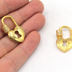 May include: Two gold heart-shaped keychains with a clear crystal accent. Each keychain has a keyhole cutout and a swivel clasp.