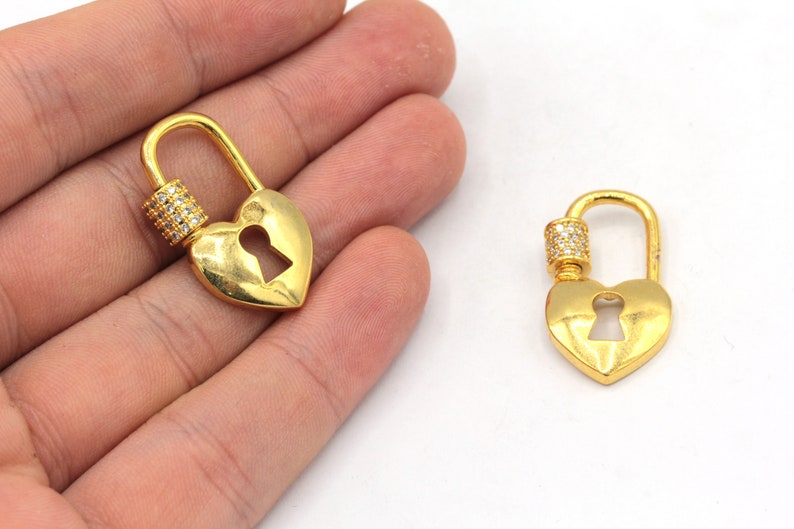 May include: Two gold heart-shaped keychains with a clear crystal accent. Each keychain has a keyhole cutout and a swivel clasp.