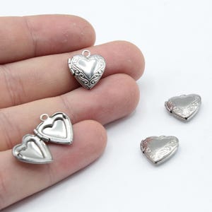 May include: Four silver heart-shaped locket charms with intricate designs. The lockets are open and ready to be filled with a special message or photo.