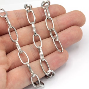May include: Three silver oval chain links on a hand. The chain links are different sizes.