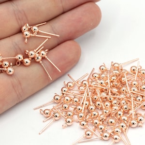 May include: A collection of rose gold-colored jewelry findings, including earring posts and decorative ball-tipped pins. The findings are small, with a polished finish, and are suitable for jewelry making and crafting projects.