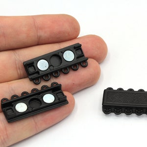 May include: Three black magnetic clasps for jewellery making. Each clasp has five loops and two magnets. The clasps are on a white surface.