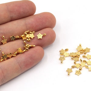 May include: Gold star-shaped metal charms with a loop for attaching to jewelry or other crafts. The charms are scattered on a white surface.