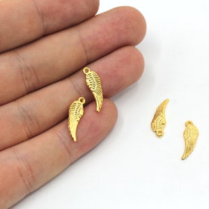 May include: Four gold-colored metal angel wing charms. The wings are detailed with a textured pattern and have a loop at the top for attaching to jewelry or other crafts.