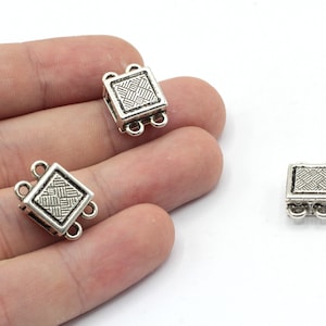 May include: Three silver-toned square-shaped clasps with a decorative pattern. Each clasp has three loops for attaching jewelry.