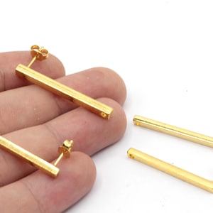 Puede incluir: Tres pares de pendientes de barra dorados con cierre de poste. Los pendientes son simples y minimalistas, con un diseño de barra recta.