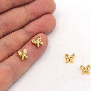 K&ouml;nnte beinhalten: Vier goldene Schmetterlingsanh&auml;nger mit klaren Kristall-Akzenten. Die Anh&auml;nger sind klein und zart und eignen sich perfekt, um Schmuck oder Bastelarbeiten mit einem Hauch von Glanz zu versehen.