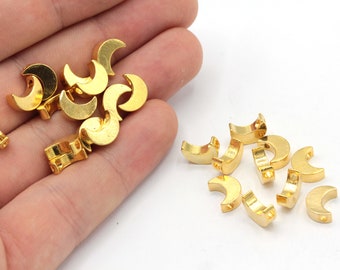 Puede incluir: Un montón de abalorios de media luna de metal dorado con un agujero para encordar. Los abalorios están esparcidos sobre una superficie blanca.
