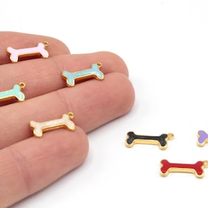 May include: A collection of colorful dog bone charms with gold-colored edges. The charms are in various colors, including pink, blue, green, white, black, purple, and red. These charms are likely used for jewelry making or crafting.