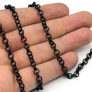 May include: Black chain necklace with a delicate, linked design. The chain is shown on a hand, highlighting its length and size.