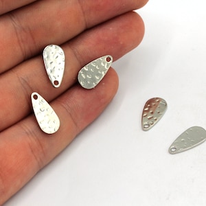 May include: Five silver teardrop-shaped metal charms with a hammered texture. Each charm has a small hole at the top for attaching to jewelry or other crafts.