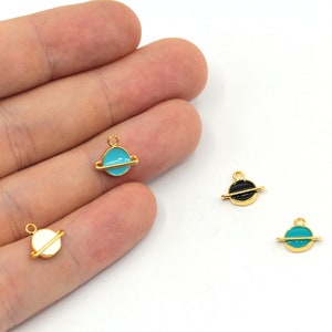 Pode incluir: Quatro pingentes dourados em forma de planetas com esmalte de diferentes cores. Os pingentes são azuis, brancos, pretos e azul-turquesa.