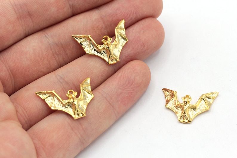 Peut inclure: Trois breloques en m&eacute;tal de couleur dor&eacute;e en forme de chauve-souris. Les chauves-souris sont en position de vol, les ailes d&eacute;ploy&eacute;es.