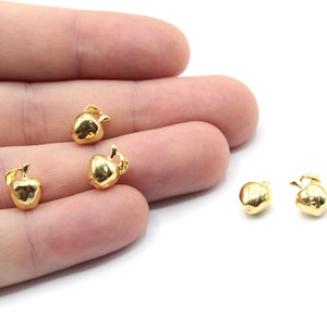 Puede incluir: Cuatro abalorios de manzana de color dorado. Los abalorios son pequeños y detallados, con un tallo y una hoja en la parte superior. Son perfectos para añadir un toque de fantasía a las joyas o las manualidades.