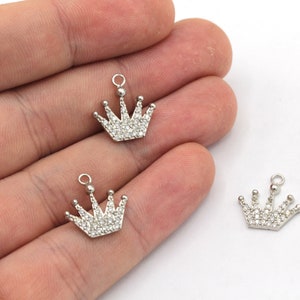 May include: Three silver crown charms with clear rhinestone accents. The charms have a loop at the top for attaching to jewelry.
