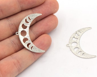 Puede incluir: Dos dijes de metal plateado en forma de media luna con un diseño recortado de las fases de la luna. Los dijes tienen un acabado cepillado.