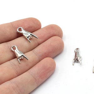 May include: Four silver metal charms shaped like a hand making the rock and roll hand gesture. The charms have a loop at the top for attaching to jewelry or other crafts.