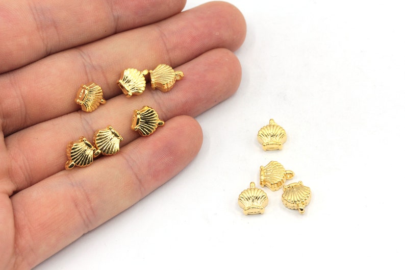 May include: A collection of ten gold-colored metal seashell charms. The charms are small and detailed, with a realistic seashell design.