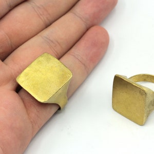 May include: Two gold-toned square signet rings. The rings are simple and have a flat, smooth surface.