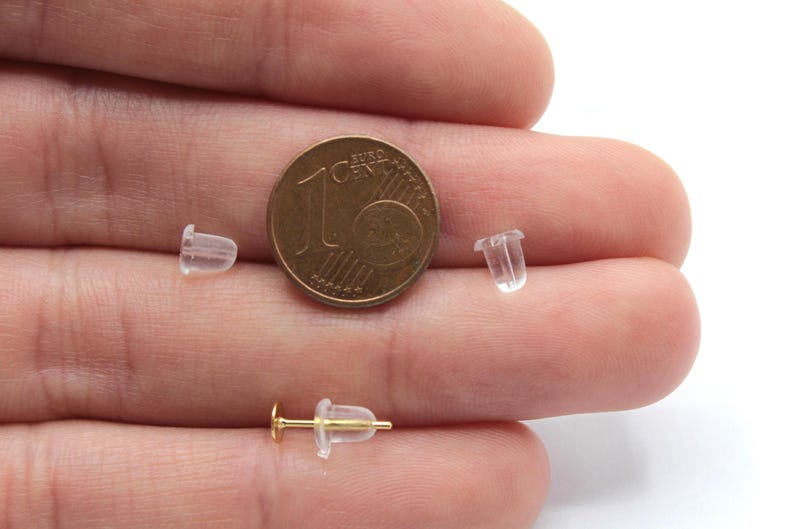 May include: Close-up of three clear plastic earring backs next to a 1 Euro coin. The earring backs are small and translucent, and the coin is a standard size.