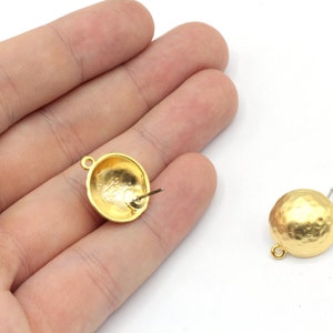 May include: Two gold-toned earring posts with a hammered texture. One earring post is shown from the side, while the other is shown from the back.