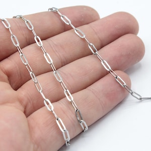 Könnte beinhalten: Eine silberne Kettenkette mit einem zarten, verlinkten Design. Die Kette besteht aus kleinen, ovalen Gliedern.