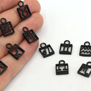 May include: A set of twelve black metal charms featuring the astrological signs. Each charm is a square with a cutout of the zodiac symbol.
