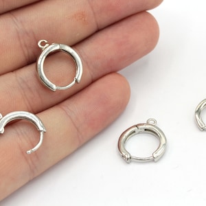 May include: Three silver hoop earring findings with a hinged closure. The findings are shown on a hand against a white background.