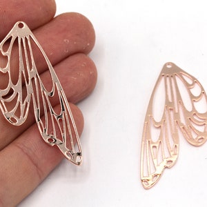 Puede incluir: Dos encantos de alas de mariposa de metal dorado rosa con un diseño delicado e intrincado. Las alas están recortadas y tienen un centro hueco.