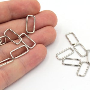 May include: A close-up of a pile of silver-toned metal D-rings. The rings are small and rectangular in shape.