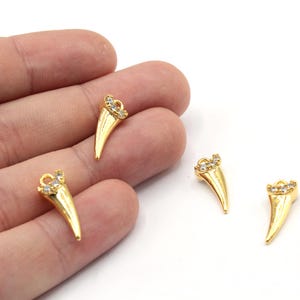 May include: Three gold-tone charms shaped like a pointed tooth with clear rhinestones. The charms have a loop at the top for attaching to jewelry.
