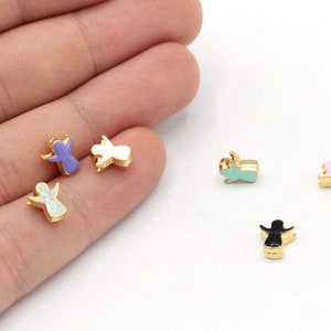 Könnte beinhalten: Fünf goldene Engelscharms mit verschiedenen emaillierten Oberflächen: lila, weiß, hellblau, rosa und schwarz.