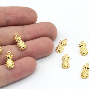 May include: A set of seven gold-toned pineapple charms. The charms are small and detailed, with a realistic pineapple design. They are perfect for adding a touch of tropical flair to jewelry or crafts.