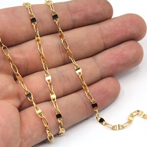 May include: A gold chain with a delicate, oval-shaped link pattern. The chain is shown on a hand, highlighting its length and size.