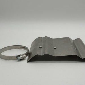 Puede incluir: Una abrazadera de metal plateado y una placa de metal plateado con dos agujeros. La placa tiene un borde ondulado.