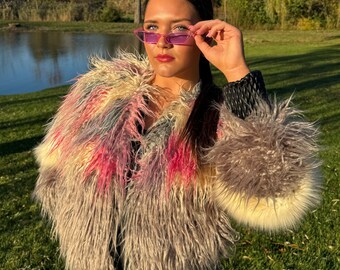 Puede incluir: Una mujer con una chaqueta de piel sintética multicolor con una cremallera negra y unas gafas de sol rosas de ojo de gato.